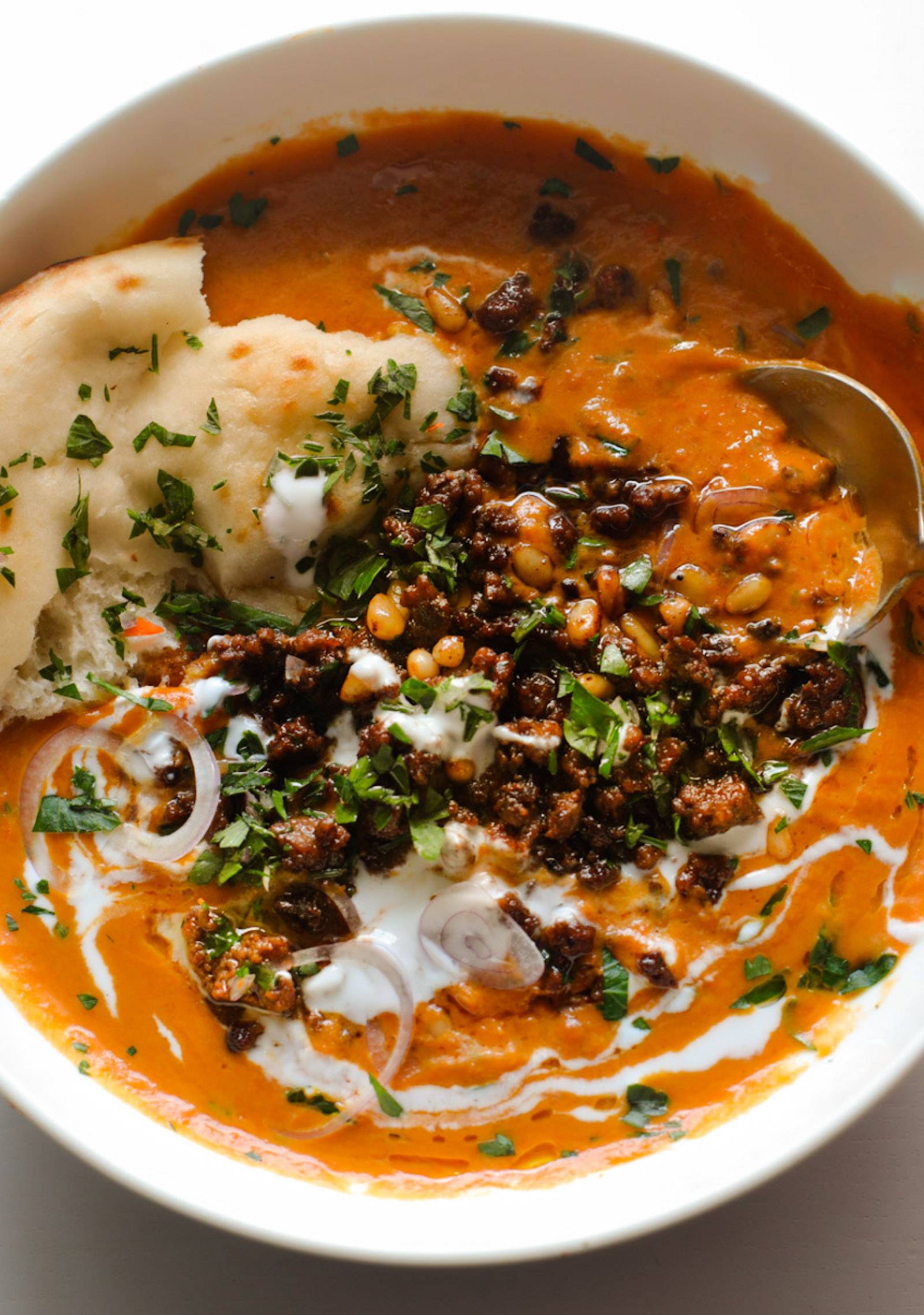 Carrot soup in a bowl topped with crispy ground beef, yogurt, and naan.
